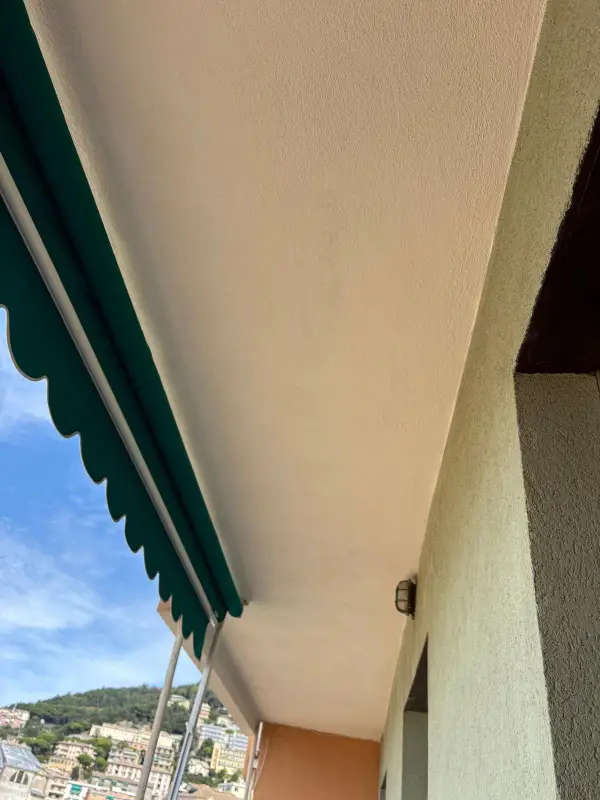 Sotto di un balcone tinteggiato e pulito, con la tenda verde e le colline sullo sfondo