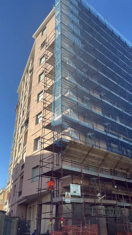 Palazzo a più piani coperto dal ponteggio con la rete blu, visto dal basso
